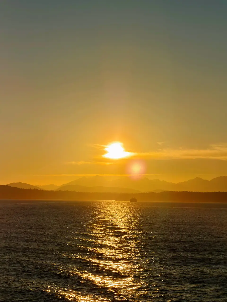 The sun setting over a sound with distant mountains
