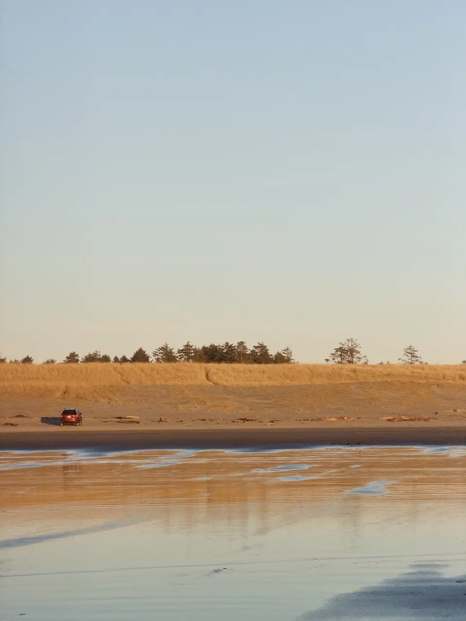 A small red car parked on a golden beach at low tide