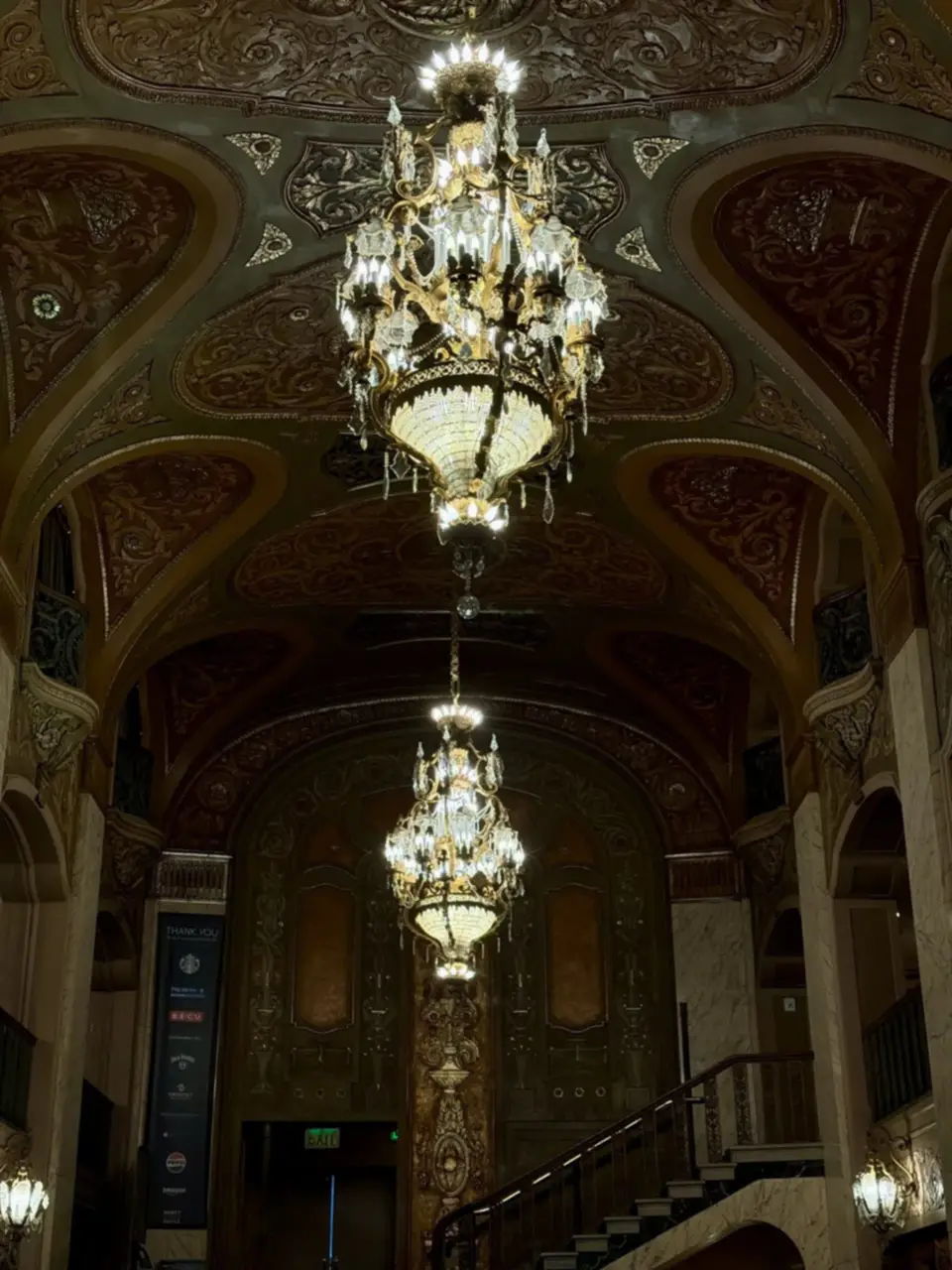 A grand staircase under glowing chandeliers in an ornate hall