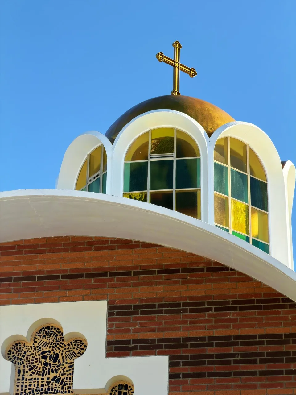 A golden cross above a white domed roof with arched windows